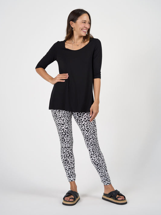 A woman stands smiling against a white background, wearing the Aretha 3/4 Sleeve Bamboo Top, white and black leopard print leggings, and black thick-soled slide sandals.