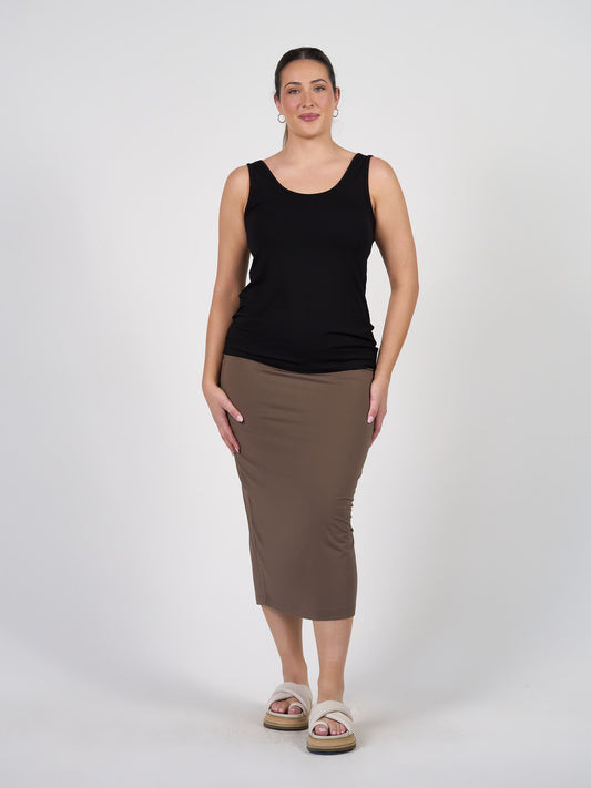 A woman poses against a white background wearing the Cindy Sleeveless Bamboo Tank Singlet in black, styled with a brown midi skirt, beige platform sandals, and hoop earrings—a wardrobe basic for effortless style.