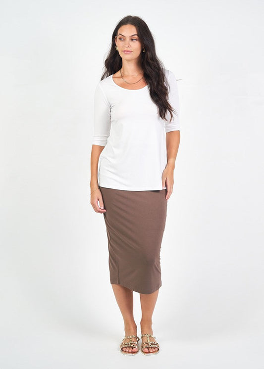 Woman with long dark hair stands against a white background, wearing the Aretha 3/4 Sleeve Bamboo Top in white, a brown midi pencil skirt, and tan sandals, with a neutral expression.