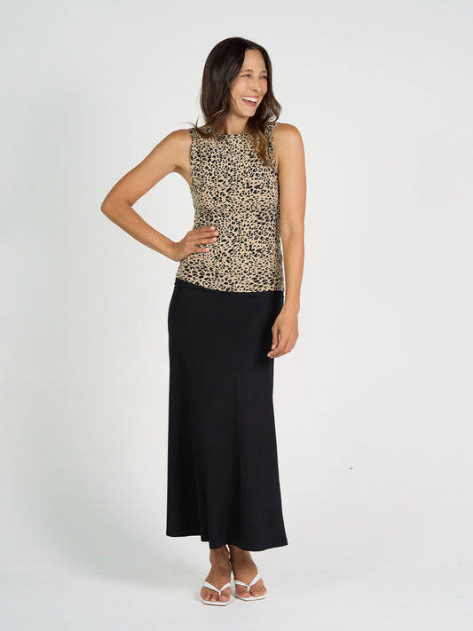 A woman smiles against a white background, wearing the Kate Bamboo Tank in leopard print with a long black skirt and white sandals. One hand rests on her hip, showcasing women's bamboo basics style.