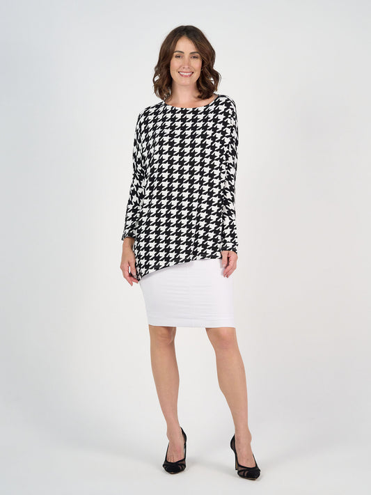A woman with shoulder-length brown hair smiles against a white background, wearing a black and white houndstooth long-sleeve top, the Midi Bamboo Whitney Tube Skirt with a stretch waistband, and black heels.