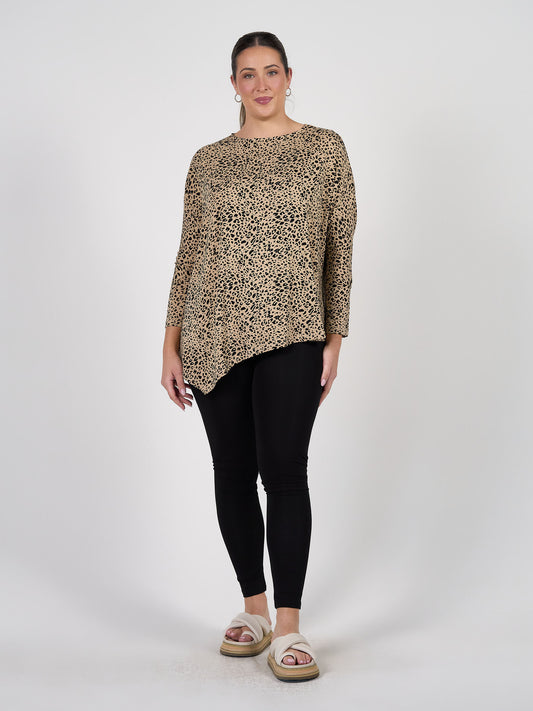 A woman stands against a plain background wearing a loose, leopard-print top with an asymmetrical hem, Luxe Bamboo Full-Length Leggings, and beige platform sandals. Her hair is pulled back and she smiles slightly.