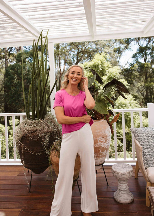Woman posing in the porch while wearing a pink plain shirt and white pants while smiling confidently (Product image)