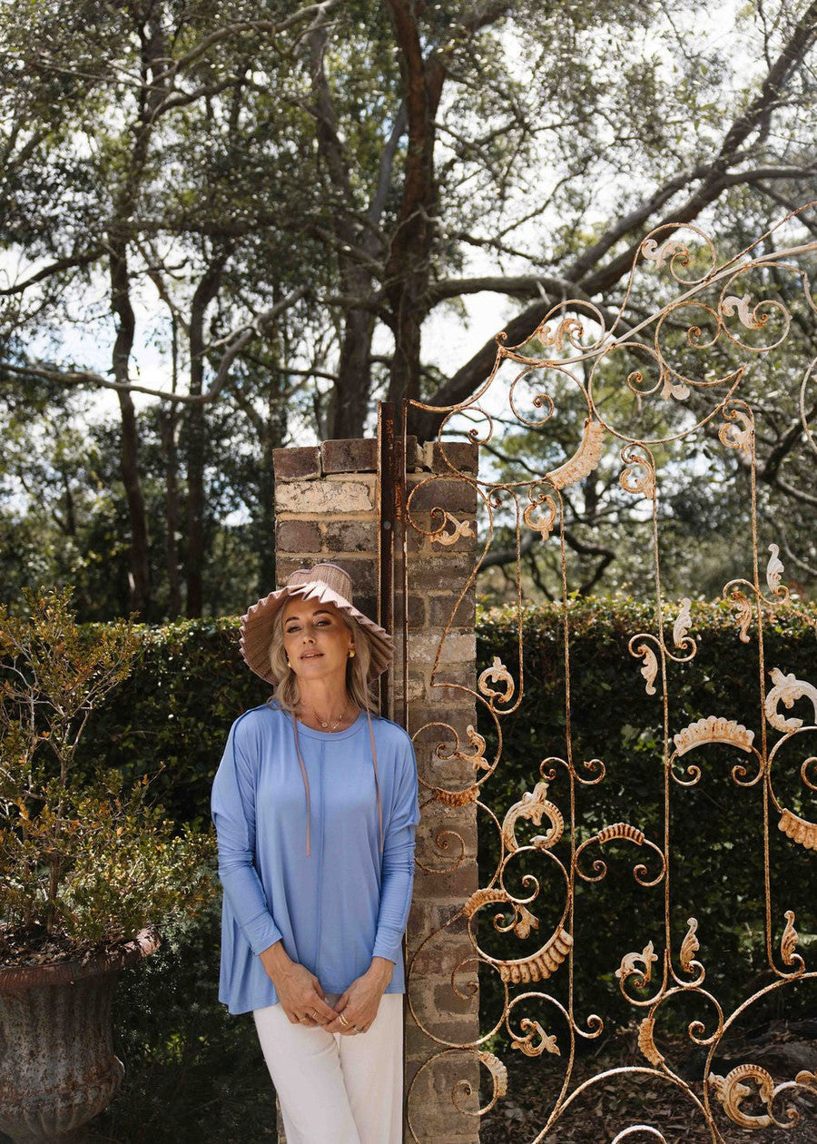 Outdoor shot of a woman wearing a long sleeve blue top, white pants and a sunhat (Product image)