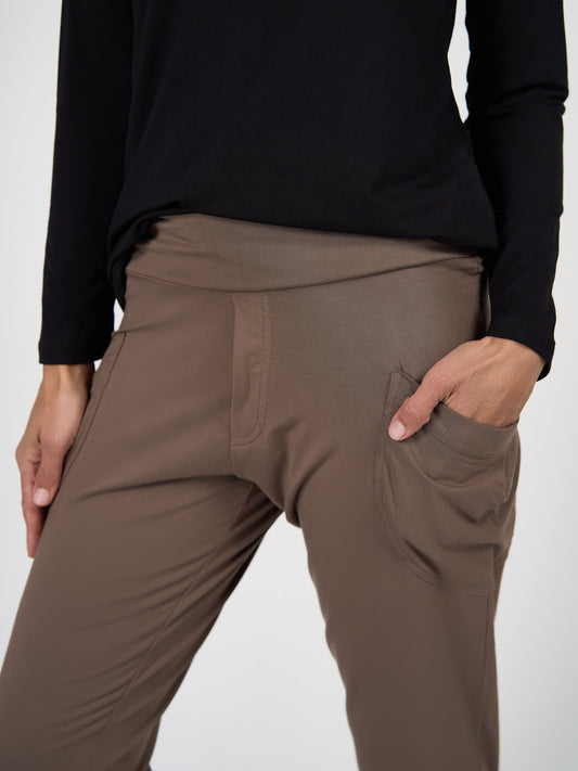 Wearing the Gaga Bamboo Cuffed Sweat Pant in Chocolate and a black long-sleeve top, a person stands with one hand in their pocket against a plain background.