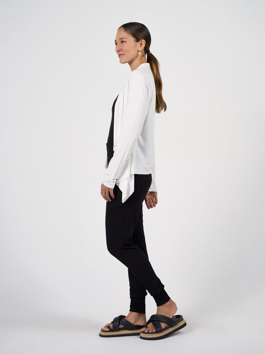 Woman in profile against a plain background, wearing the Joni Bamboo Waterfall Cardigan/Jacket in cream over a black top and black pants with black platform sandals. Her long brown hair is tied back in a low ponytail.