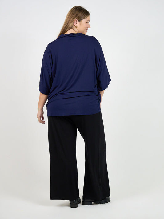 A woman with long hair, seen from behind, wears the Alanis 3/4 Sleeve Collared Bamboo Shirt in navy and black wide-leg pants, standing against a plain white background.