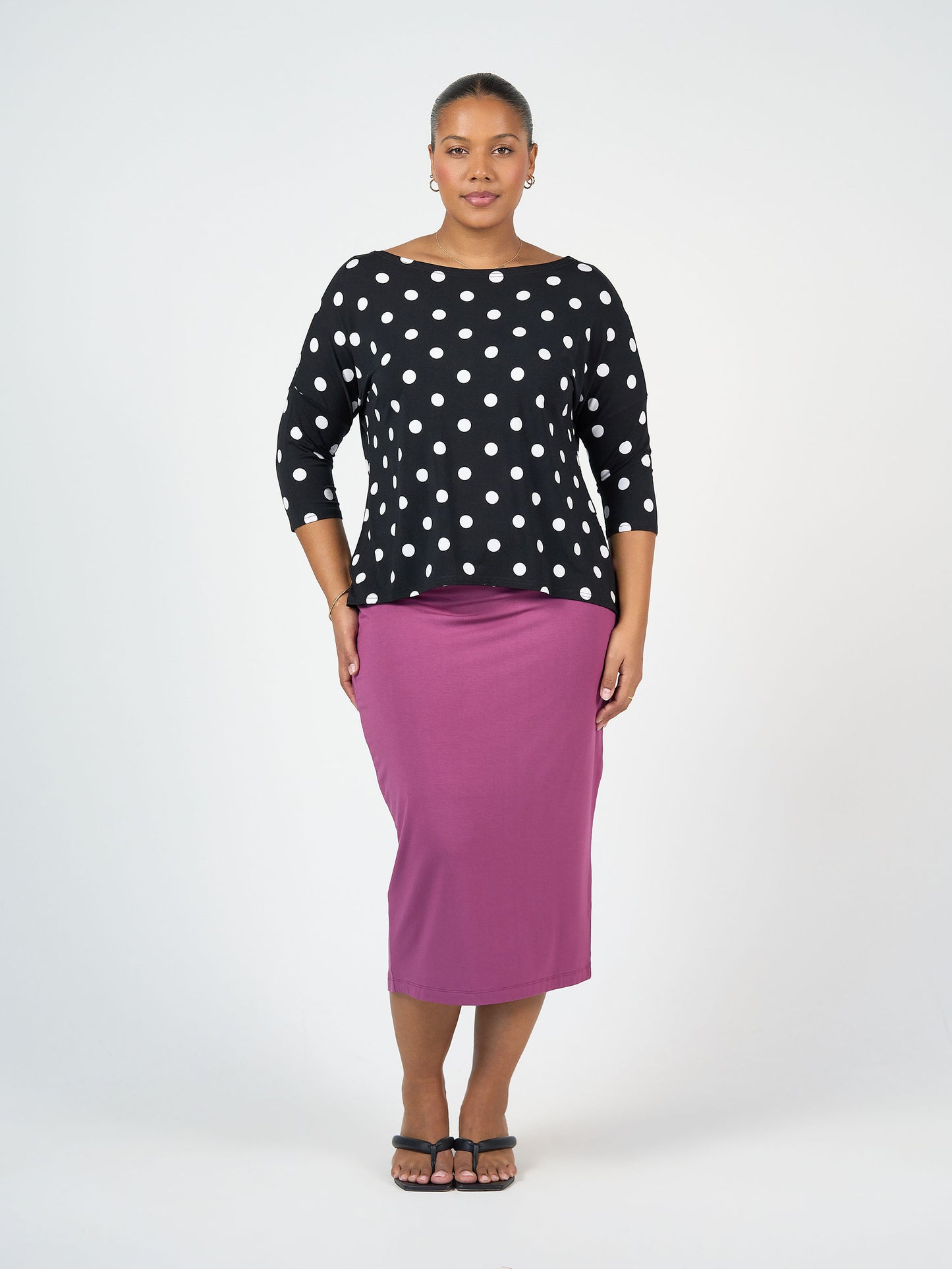 A woman faces forward in a black top with white polka dots, the Maxi Bamboo Whitney Tube Skirt in Plum, and black sandals. The background is plain white.