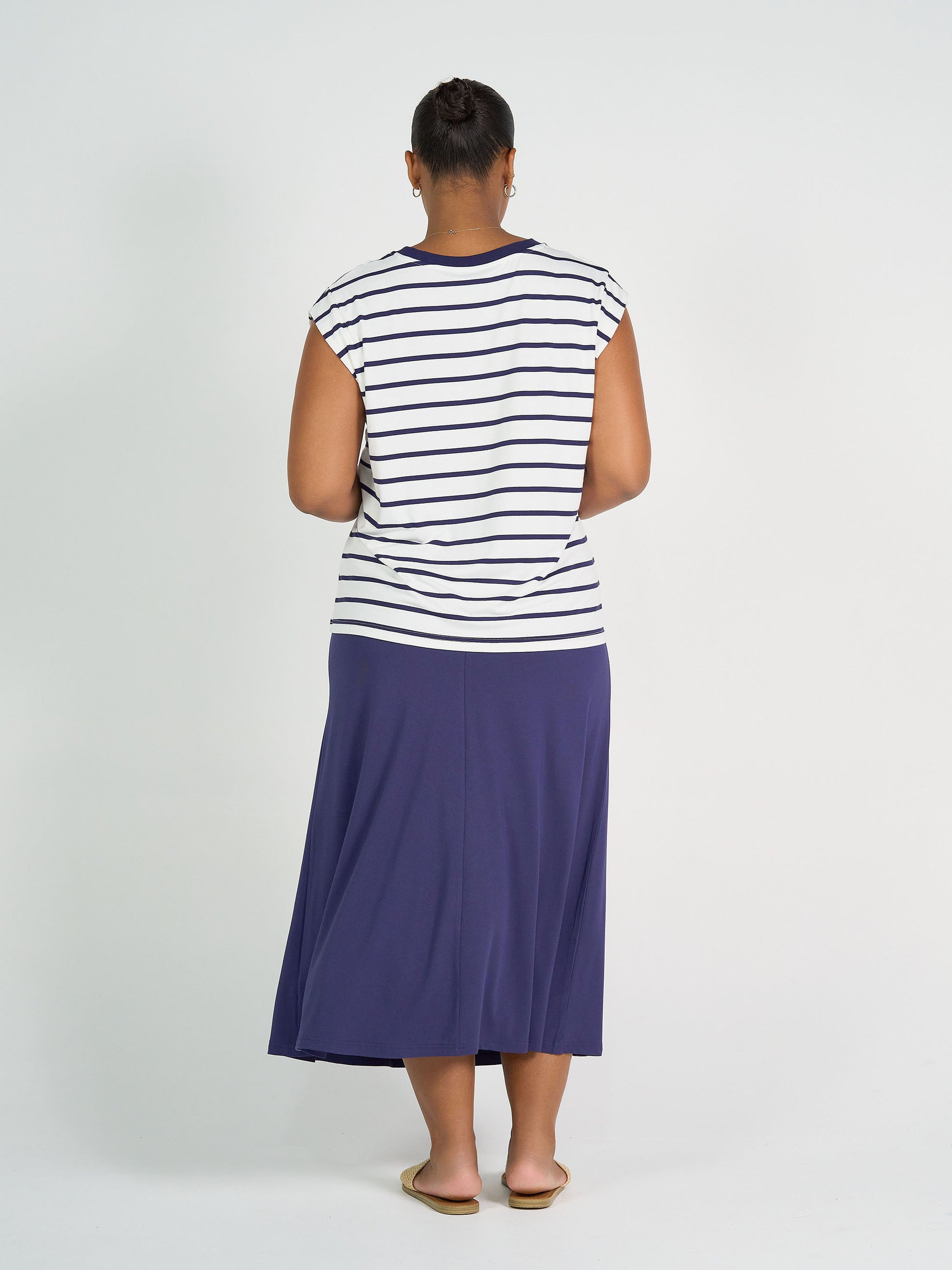 A person models the Donna Cap Sleeve Bamboo Tee in blue & white stripe, paired with a navy midi skirt and beige flats, against a plain white background—ideal for everyday wear.