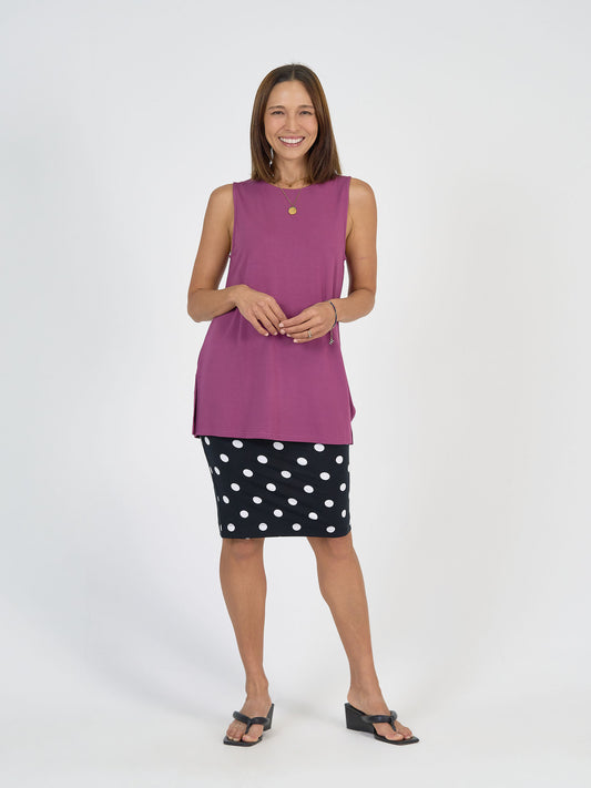 A woman smiles in a sleeveless purple top, the Midi Bamboo Whitney Tube Skirt in polka dot with a stretch waistband, and black heeled sandals against a plain white background.