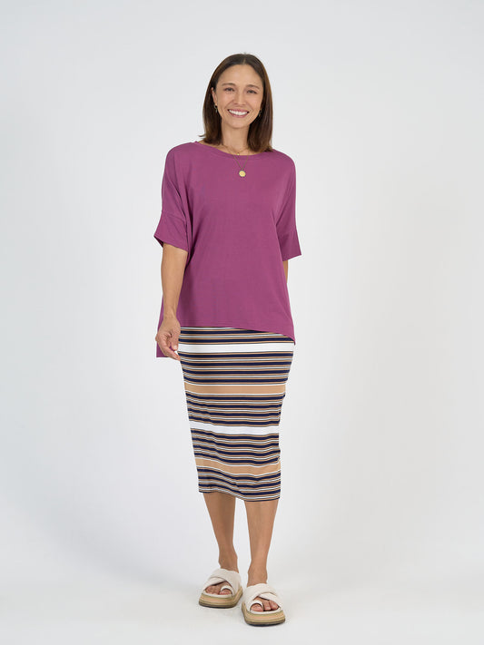 A woman smiles against a white background, wearing a loose purple top, white sandals, and the Maxi Bamboo Whitney Tube Skirt - Stripe.