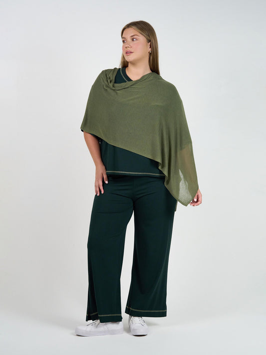 A woman stands against a plain background wearing the Carey Bamboo Culotte in dark green with a matching top, an olive green shawl over her shoulders, and white sneakers. She gazes to the side with a relaxed expression.