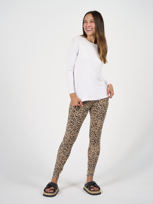 A woman stands smiling against a white background, wearing the Jones Long Sleeve Fitted Bamboo Top, leopard print leggings, and black sandals with thick soles.