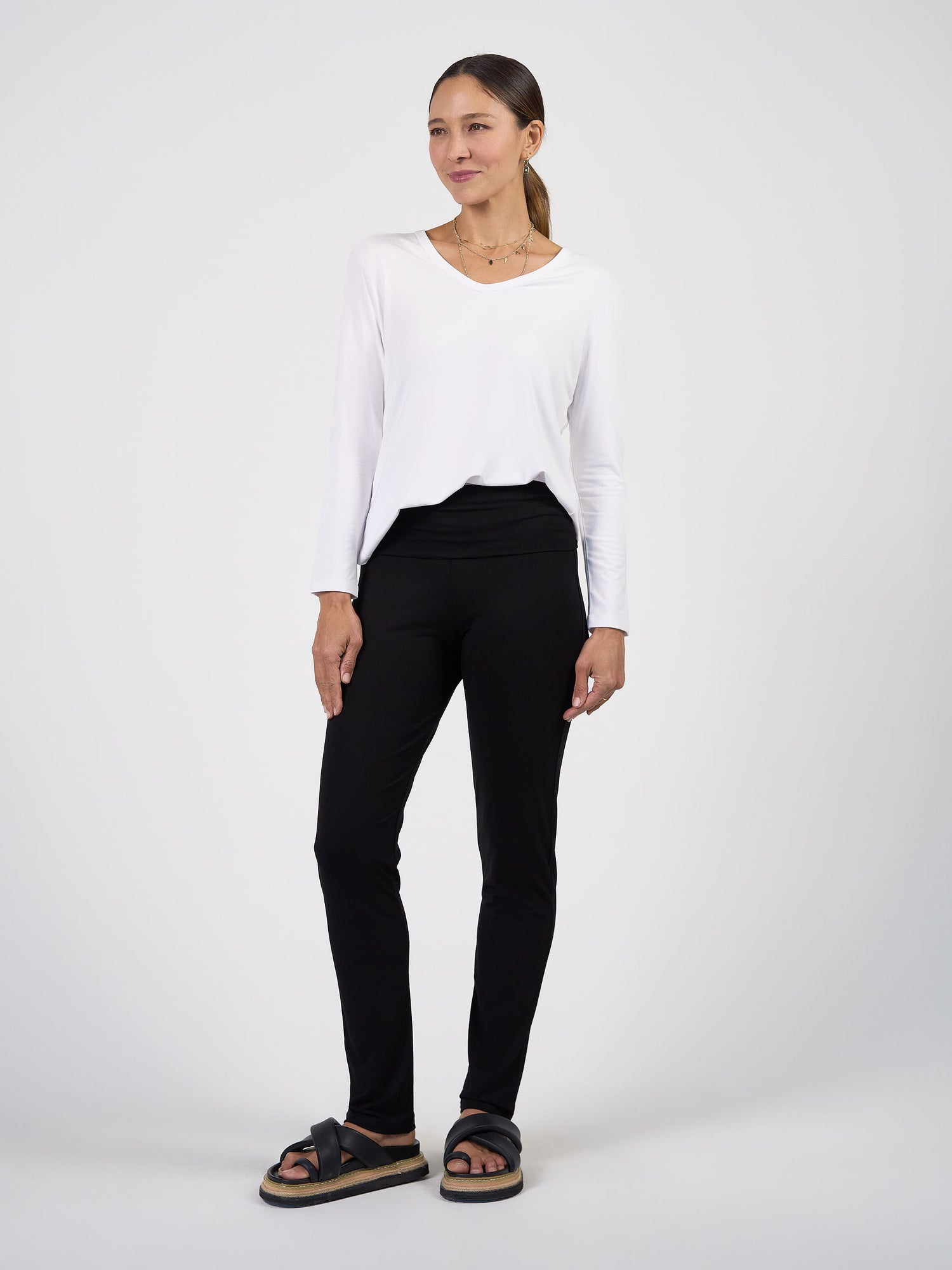 Woman wearing a white long-sleeve top and black pants on a white background