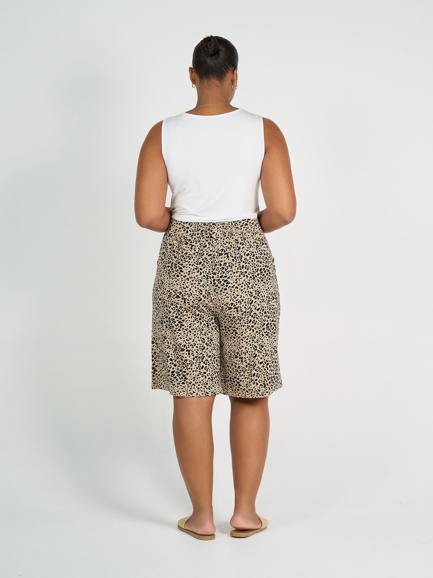 A person faces away from the camera, wearing the Kate Bamboo Tank and knee-length leopard print shorts with beige flat shoes, set against a plain white background.