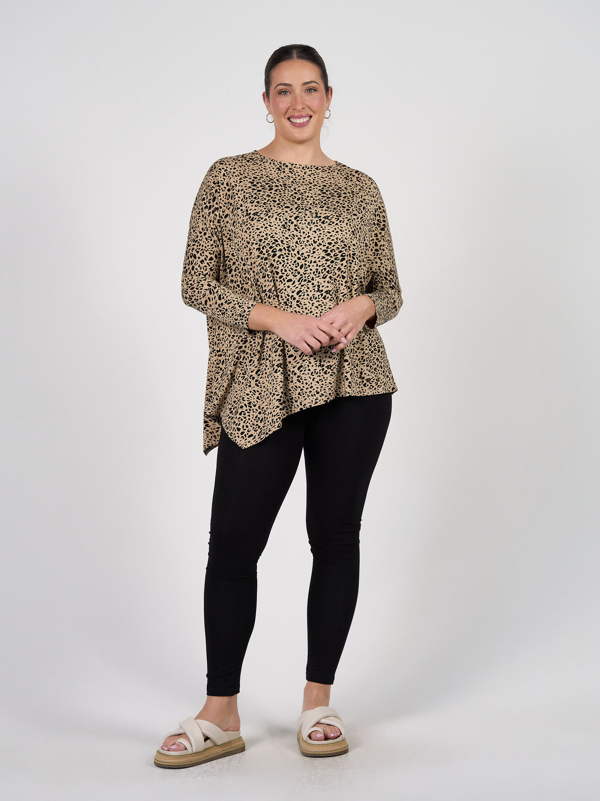 A woman with her hair pulled back smiles against a white background, wearing a loose leopard-print top, beige slide sandals, and Luxe Bamboo Full-Length Legging in black. She stands with one hand resting on her hip.