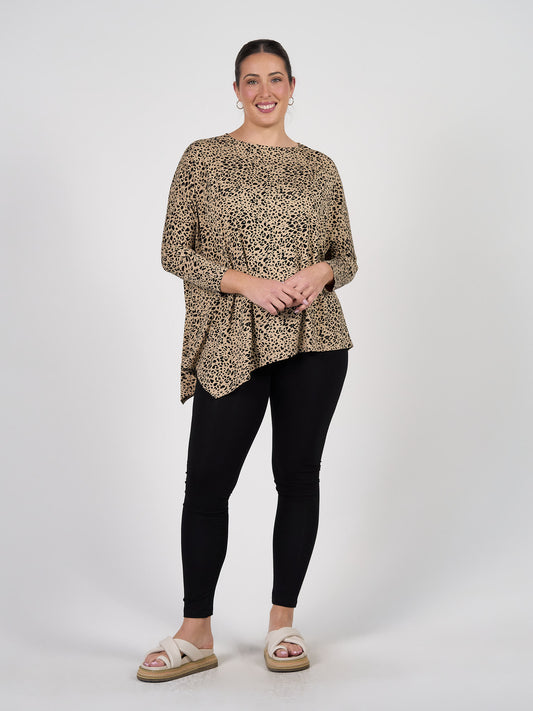 A woman with her hair pulled back smiles against a white background, wearing a loose leopard-print top, beige slide sandals, and Luxe Bamboo Full-Length Legging in black. She stands with one hand resting on her hip.