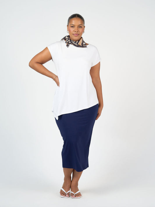 A woman poses against a plain background wearing a white short-sleeve top, navy blue midi skirt, white sandals, and the Benni Bamboo Scarf - Stripe—an elegant sustainable accessory—tied around her neck.