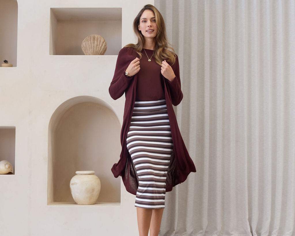 Woman wearing a burgundy cardigan over a striped dress in a minimalistic room.